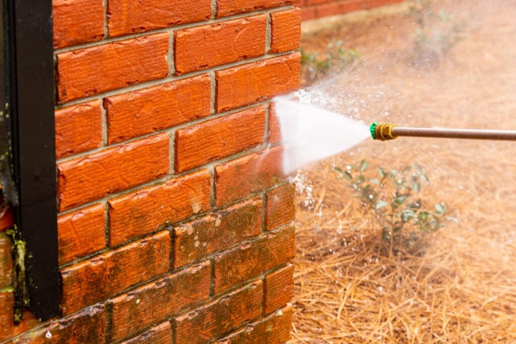 A person using a hose to clean the side of a brick wall.