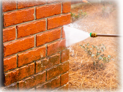 A person is spraying water on the side of a brick wall.